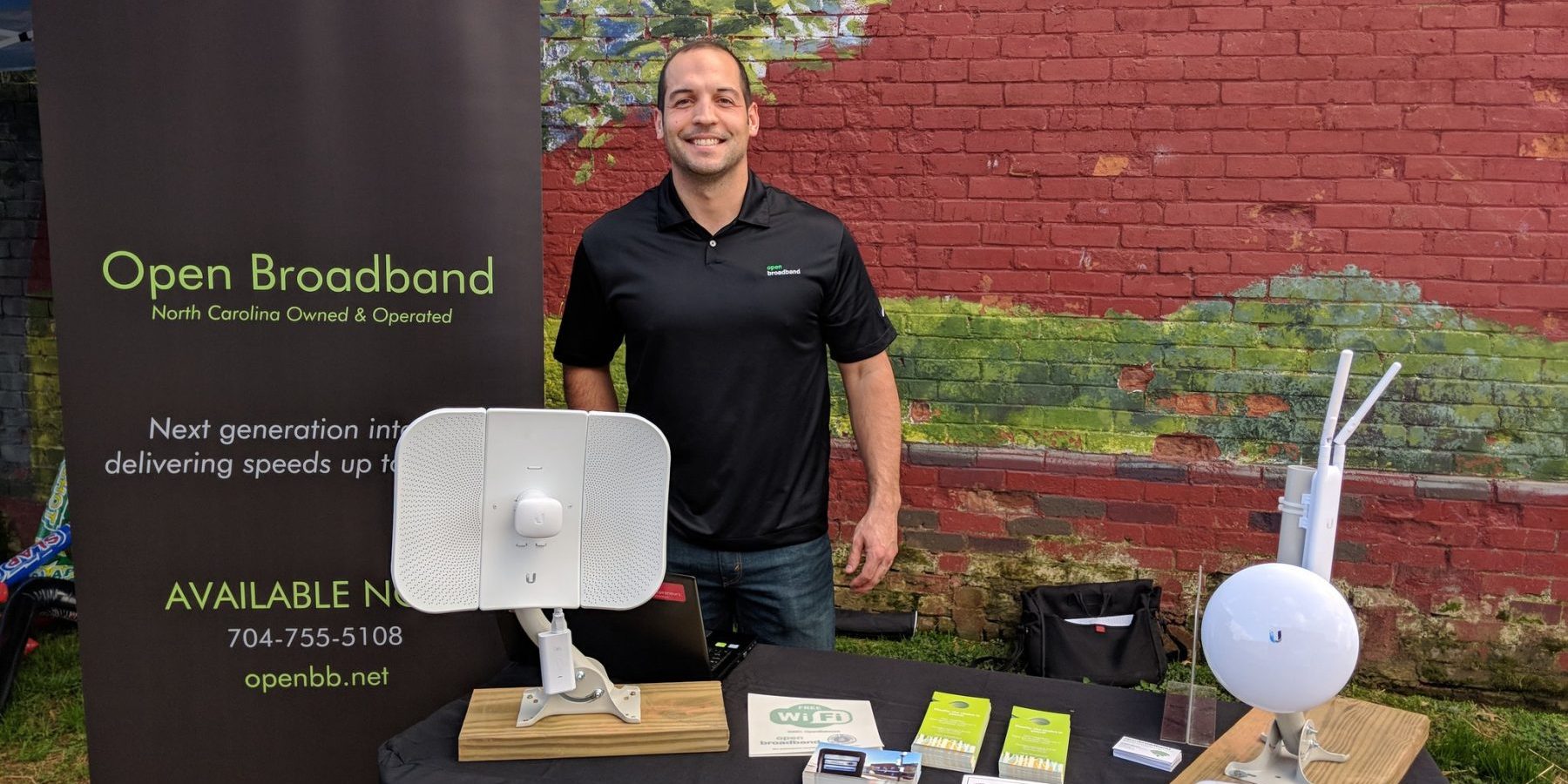 Man standing with open broadband banner and table full of devices and flyer